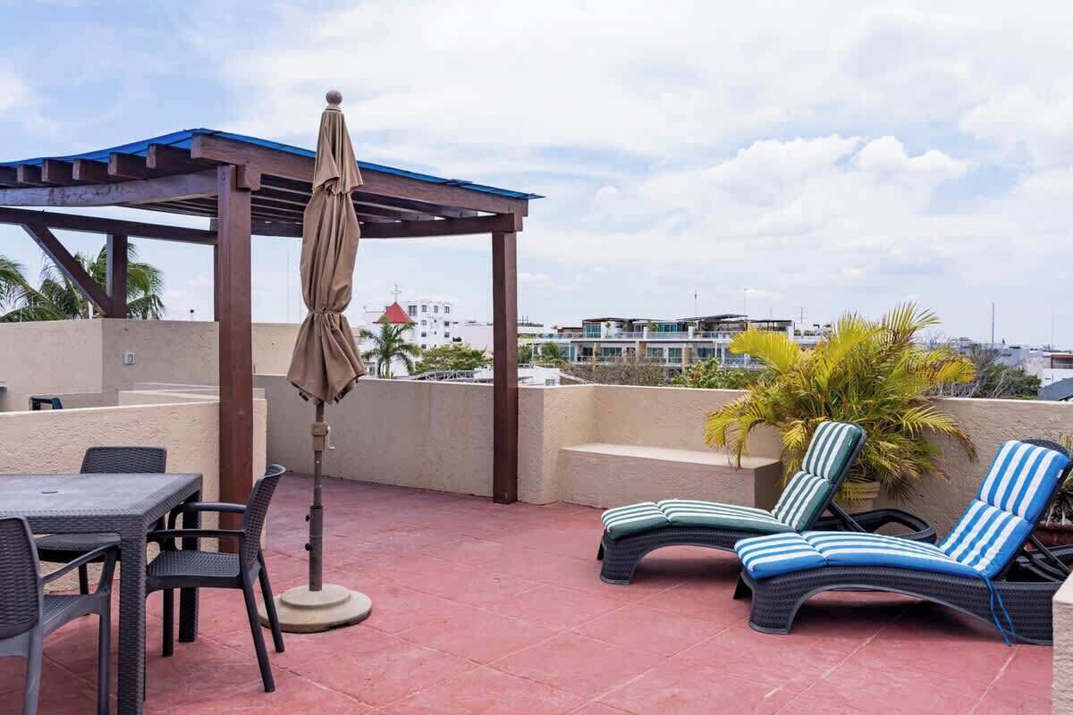 A rooftop terrace with a pergola, lounge chairs, a table, and chairs.