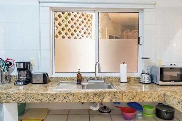 A kitchen with a granite countertop, a coffee maker, a toaster, a sink, a microwave, and a window with a lattice screen.