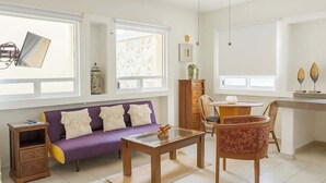 A living room with a purple sofa, a wooden coffee table, and a dining area with a chair and a small table.
