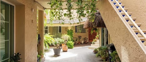 A covered outdoor area with potted plants, a staircase, and a thatched roof structure.