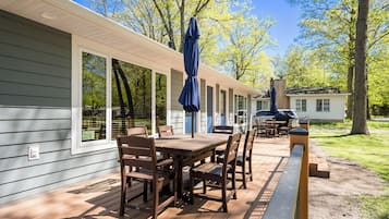 Une terrasse en bois avec une table et des chaises, un parasol et une vue sur une maison et des arbres.