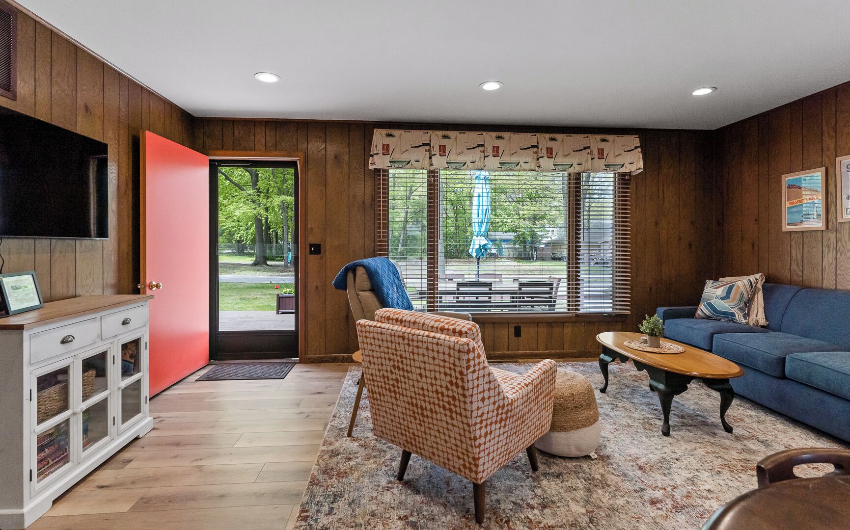 Un salon avec un plancher en bois, un canapé bleu, un fauteuil à motifs, une table basse et un téléviseur posé sur un meuble.