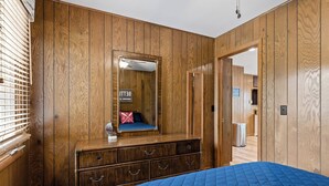 A bedroom with wooden paneling, a large bed with a blue quilt, a dresser with drawers, a mirror, and a sign indicating a bathroom with a lake view. - Awesome Silver Lake Rental - Short Distance to Lake MI (Mears)