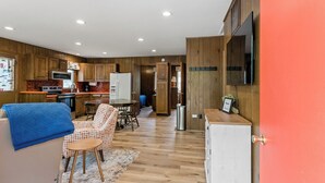 A compact kitchen with wooden cabinets, a microwave, and a refrigerator. There is a dining area with a table and chairs, and a small rug on the floor. - Awesome Silver Lake Rental - Short Distance to Lake MI (Mears)