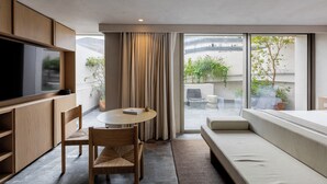 Een moderne kamer met een flatscreen-tv, houten meubels, een ronde tafel, een bank en grote ramen voorzien van gordijnen.