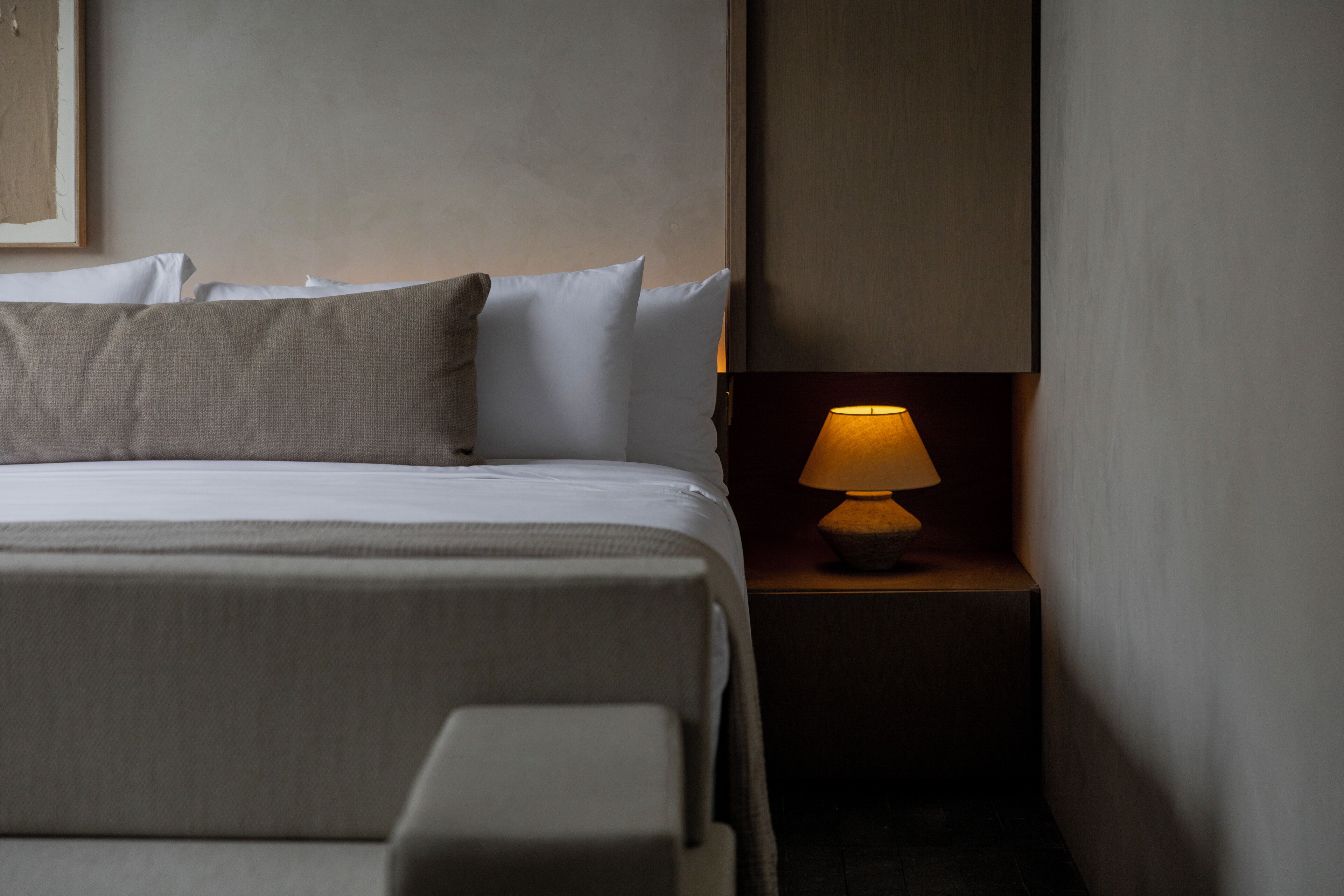 A neatly made bed with pillows, a bedside lamp, and a wall-mounted artwork.