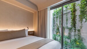 A hotel room with a large bed, a bedside table, and a view of greenery through a sliding glass door. - Lamartine  (Mexico City)