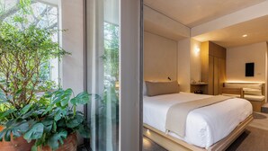 Een moderne hotelkamer met een groot bed, een nachtkastje, en een plant in pot bij het raam.