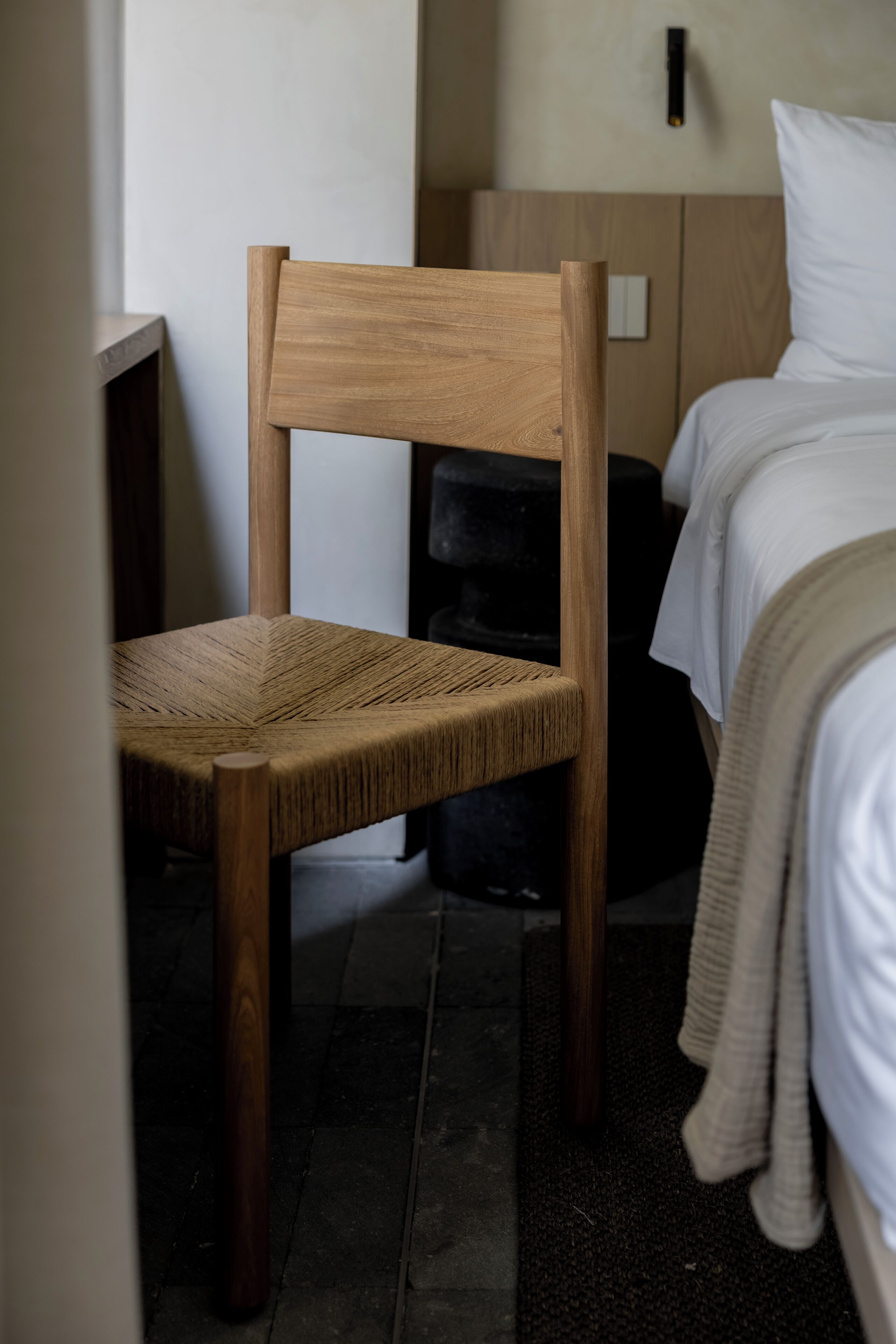 Una silla de madera con asiento y respaldo de mimbre, ubicada en una habitación con una cama y una mesita de noche.