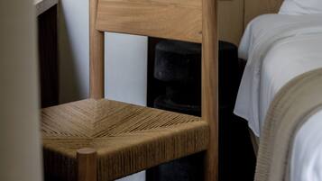 Una silla de madera con asiento y respaldo de mimbre, ubicada en una habitación con una cama y una mesita de noche.