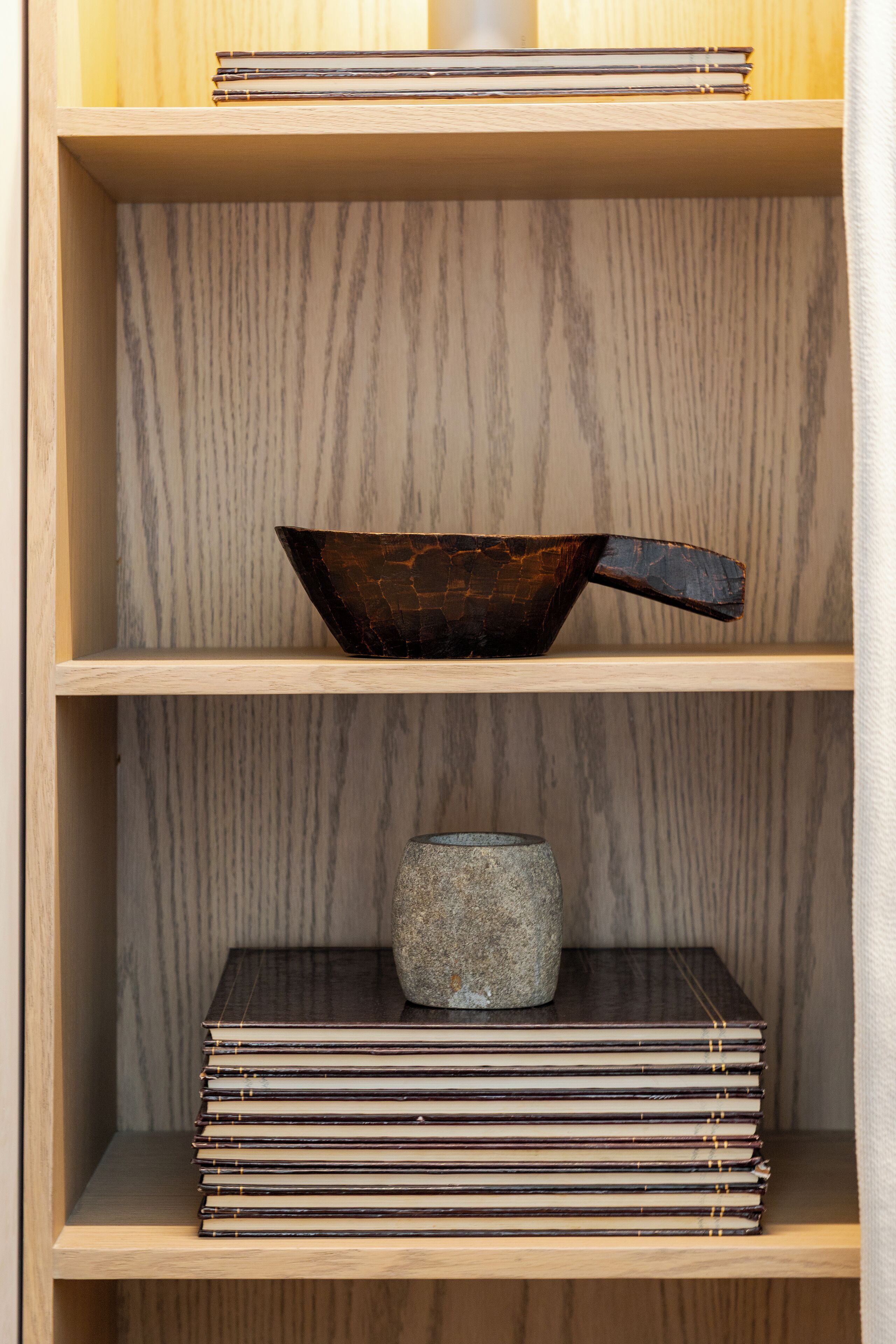 A wooden shelf with a dark bowl and a stone container.