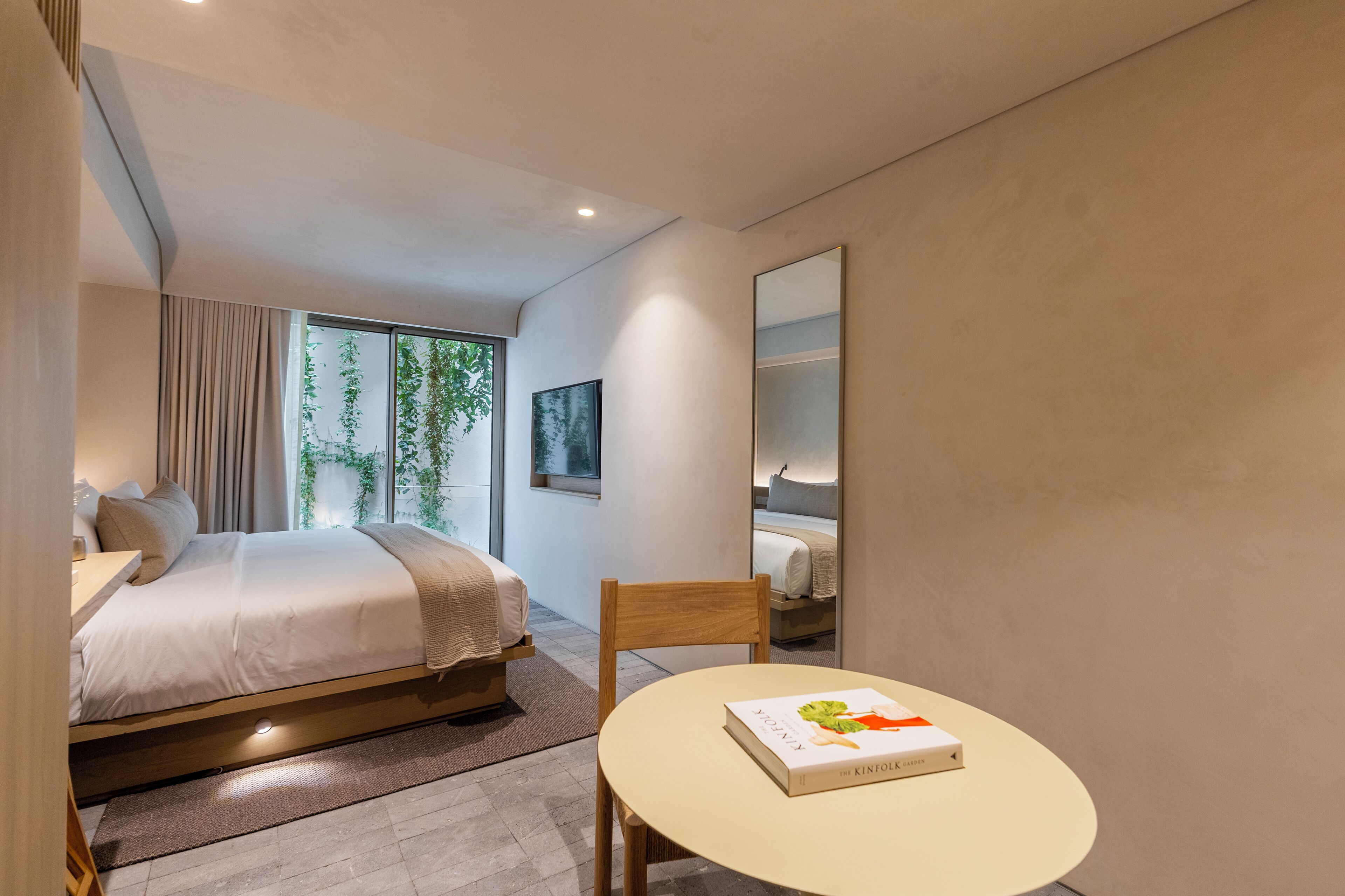 Un dormitorio moderno con cama, mesita de noche y una pequeña mesa redonda con un libro.