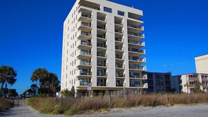 Un hotel de varios pisos con balcones, situado cerca de una playa con palmeras.