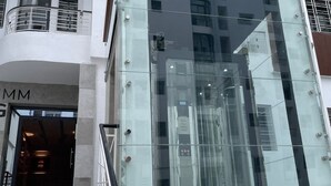 A modern building with a glass facade, a visible elevator, and a staircase leading to a door labeled "MM". - Flat in tanger : wifi, prvt parking, air-co netflix... (Tanger)