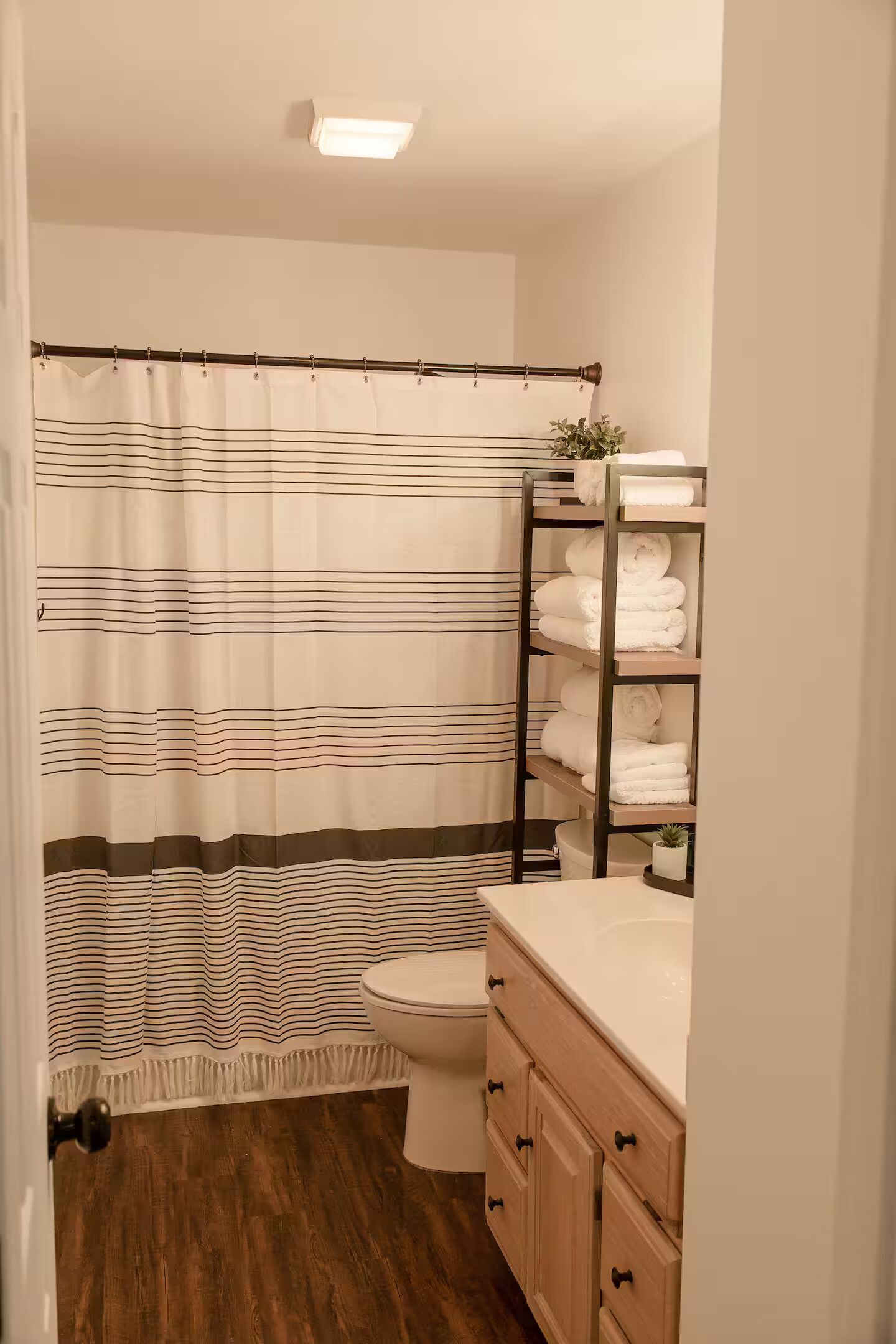 A bathroom with a striped shower curtain, a toilet, a wooden vanity with a sink, and a towel rack with folded towels.