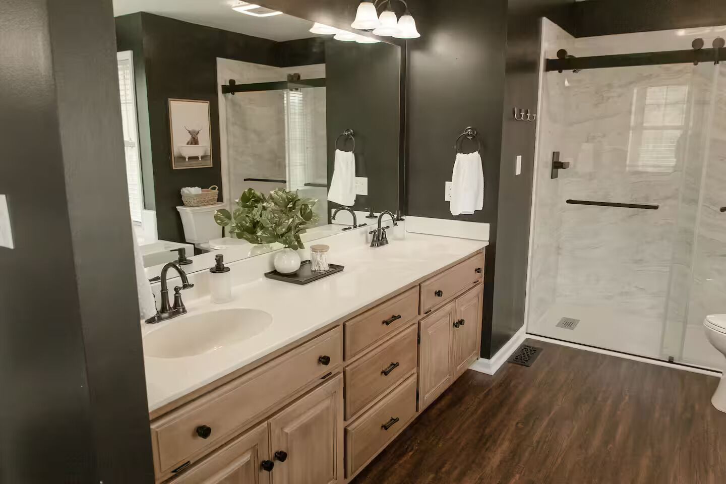 A modern bathroom with a large mirror, dual sinks, and a walk-in shower.