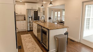 A modern kitchen with white cabinets, stainless steel appliances, a granite countertop, and a large window. - Lake Blackshear Retreat! (Cordele)