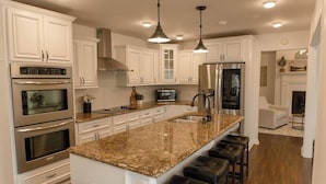 A modern kitchen with white cabinetry, stainless steel appliances, a granite countertop, and bar stools. - Lake Blackshear Retreat! (Cordele)