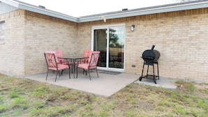 Une terrasse extérieure avec un mur en briques, une porte-fenêtre coulissante, un barbecue et une table avec des chaises.