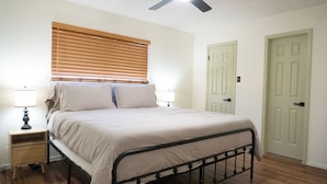 Une chambre à coucher avec un lit, des tables de chevet, un ventilateur de plafond et une fenêtre avec des stores.
