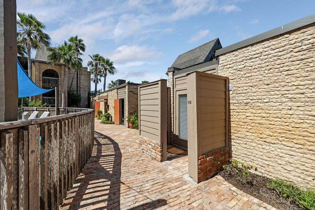 A brick pathway leading to a building with a stone wall and a wooden fence.
