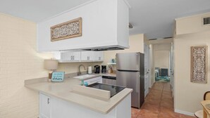 Cocina compacta con armarios blancos, refrigerador de acero inoxidable y lavavajillas integrado.