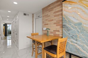 A dining area with a wooden table and chairs, a marble wall, and a door leading to another room. - Beachfront Family-Friendly Condo w/ Heated Pool! (South Padre Island)