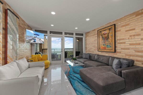 A modern living room with a white sofa, a gray sofa, and a yellow armchair. There is a large painting on the wall and a flat-screen TV mounted on the wall. - Beachfront Family-Friendly Condo w/ Heated Pool! (South Padre Island)