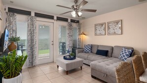 Ein Wohnzimmer mit Sofa, Hocker, Deckenventilator und Fernseher.