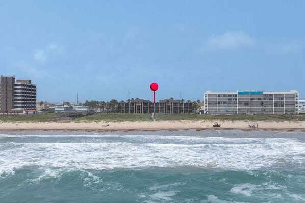 Un hotel frente a la playa con un punto de referencia rojo, playa de arena y olas oceánicas.