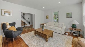 A living room with a sofa, armchair, coffee table, and a staircase leading to another room. - Spacious Central Berkshires Home for Groups (Lee)