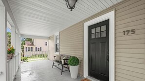 A porch with a bench, a potted plant, and a black door with the number 175. - Spacious Central Berkshires Home for Groups (Lee)