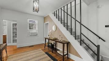 Un interior moderno con una escalera, piso de madera, una consola y una lámpara colgante.