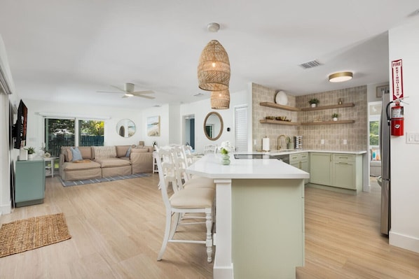 A modern kitchen with a central island, light wood flooring, and a dining area with white chairs.
