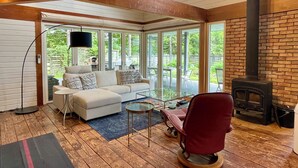 A cozy living room with a sofa, a glass coffee table, and a red chair. There is a fireplace and a TV mounted on the wall. - GARDEN SHED (Yamanakako)