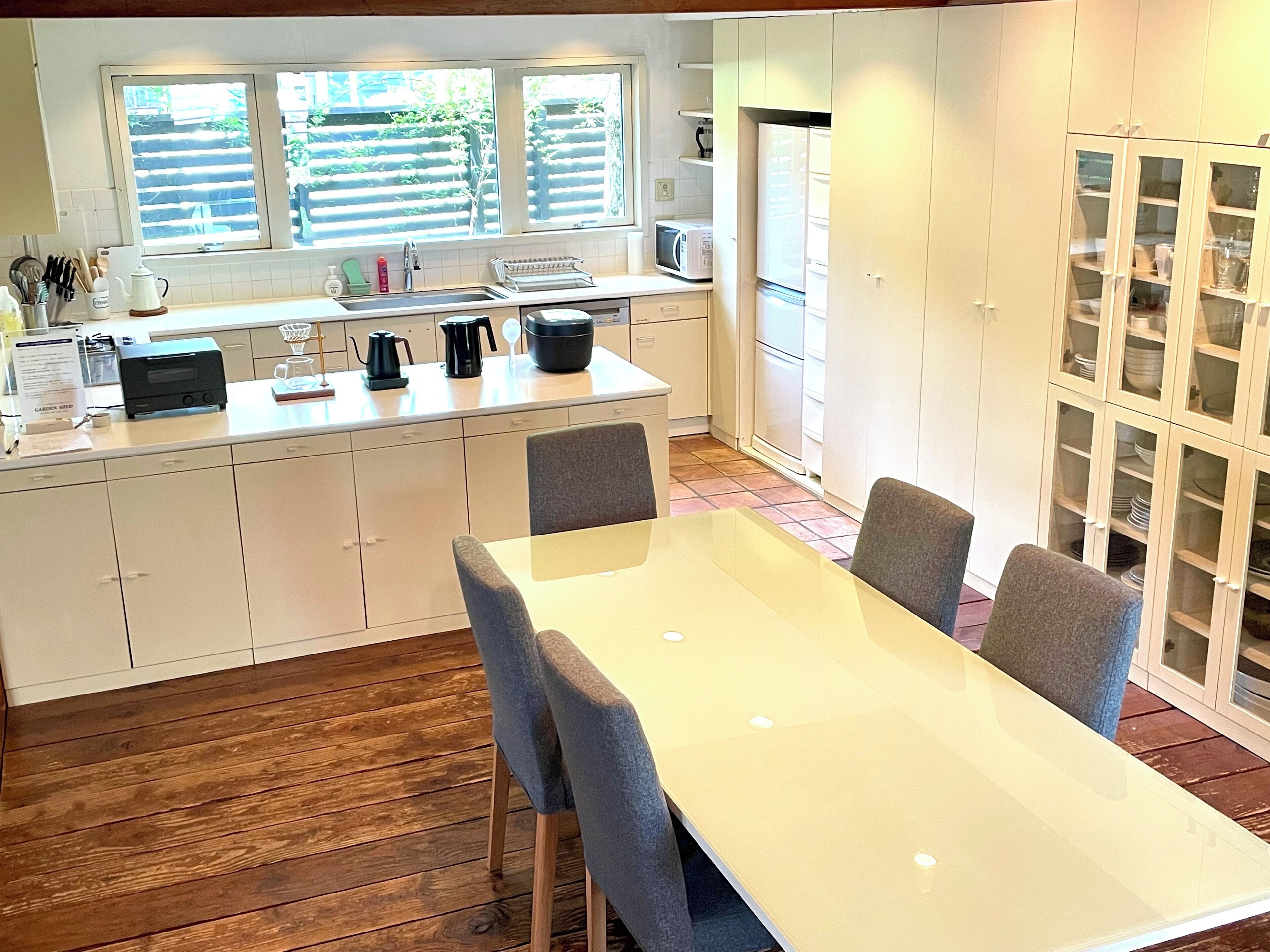 A modern kitchen with white cabinets, a dining table with four chairs, and a window with blinds.