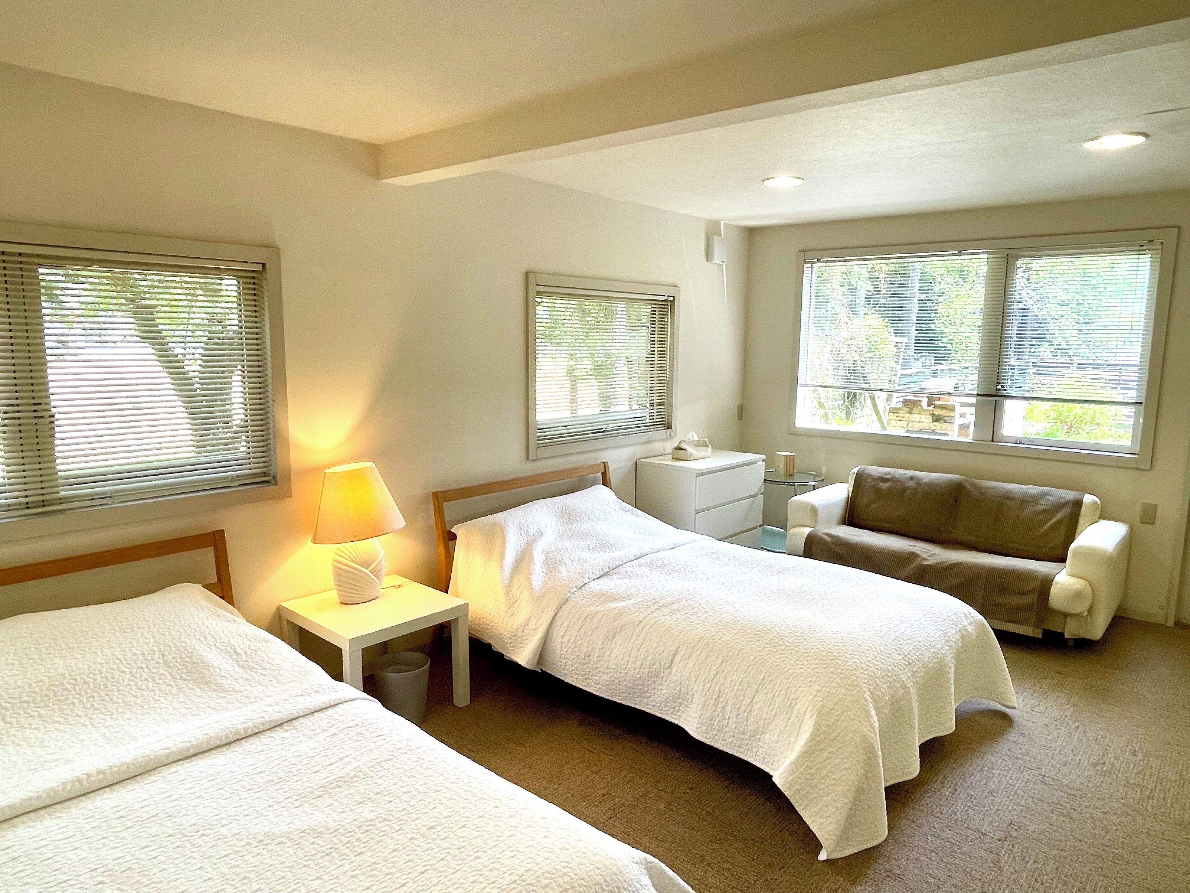 A hotel room with two beds, a nightstand, a lamp, a small table, and a sofa.