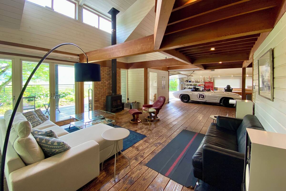 A spacious living area with a high ceiling, a fireplace, and a classic car in the background.
