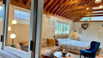 A cozy room with a bed, a sofa, a coffee table, and a chair. There are windows and a wooden ceiling.