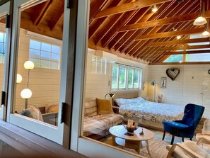 A cozy room with a bed, a sofa, a coffee table, and a chair. There are windows and a wooden ceiling. - GARDEN SHED (Yamanakako)