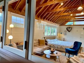 Habitación acogedora con cama, sofá, mesa de centro y una silla. Se observan ventanas y un techo de madera.