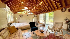 A cozy room with a bed, a blue armchair, a round wooden table, and a patterned rug. - GARDEN SHED (Yamanakako)