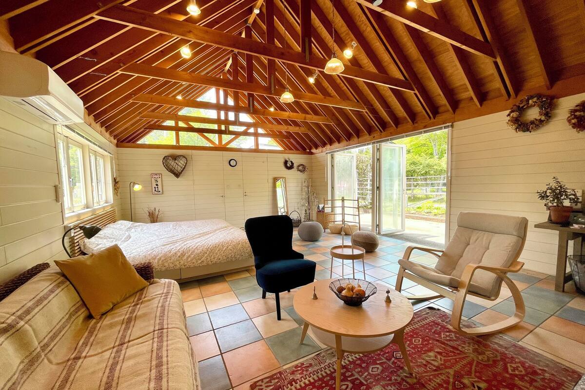 A cozy room with a bed, a blue armchair, a round wooden table, and a patterned rug.