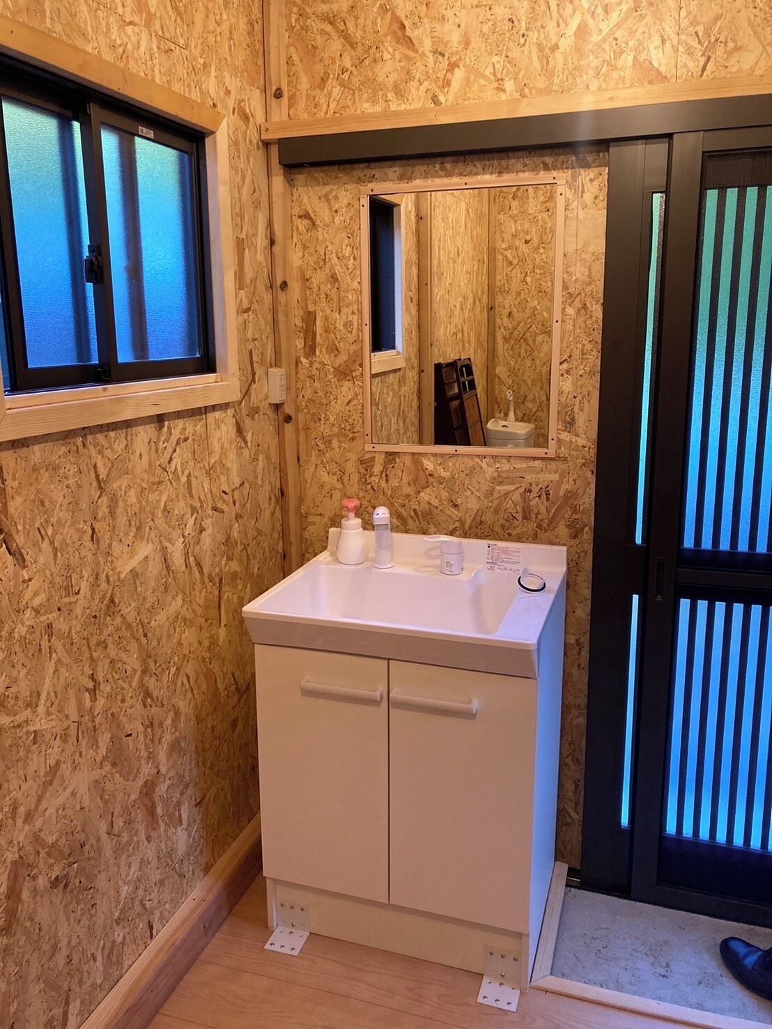 A bathroom with a wooden wall, a white sink, a mirror, and a window.