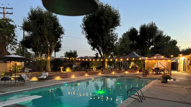Una piscina con mobili da patio circostanti, un gazebo e luci a catena.