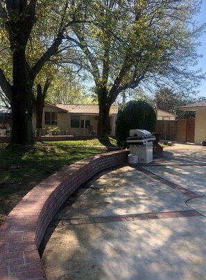 Un camino de entrada residencial con bordillo de ladrillo, una parrilla techada y una casa con garaje.