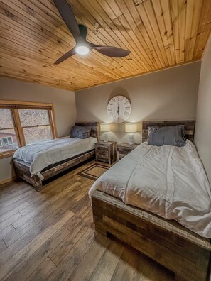 A bedroom with two wooden beds, a ceiling fan, a wall clock, and a window.