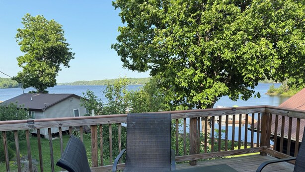 Eine Terrasse mit Tisch und Stühlen, mit Blick auf einen See, im Hintergrund ein Haus.