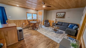 Une pièce aux murs lambrés, comprenant une table à manger, des chaises, un canapé, une petite table et un ventilateur de plafond.