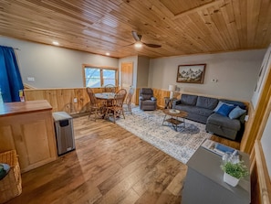 A wooden-paneled room with a dining table, chairs, a sofa, a small table, and a ceiling fan.